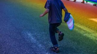 Junge Person laeuft mit Transflagge auf Asphalt, der in Regenbogenfarben scheint