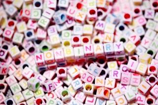In einem Meer aus Buchstabenperlen ist das Wort Nonbinary im Zentrum gelegt In einem Meer aus Buchstabenperlen ist das Wort Nonbinary im Zentrum gelegt
