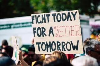 Im Bild ist eine Demonstration zu sehen, im Fokus steht ein Plakat auf dem steht: FIGHT TODAY FOR A BETTER TOMORROW