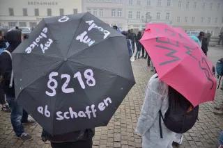 Zwei Personen mit Regenschirmen stehen mit dem Rücken zur Kamera. Auf einem Regenschrim steht §218 abschaffen.