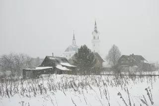 The Church of Archangel Michael in Podzhigorodovo Häuser, Scheunen und Kirche eines russischen Dorfes im Schneeschauer