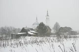 Häuser, Scheunen und Kirche eines russischen Dorfes im Schneeschauer