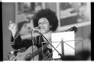 Fasia Jansen Dia Sängerin Fasia Jansen steht mit Gitarre hinter einem Notenständer und Mikrofon