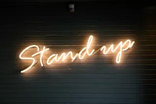 Leuchtzeichen mit der Schrift "Stand up" frontal fotografiert vor dunklem Hintergrund