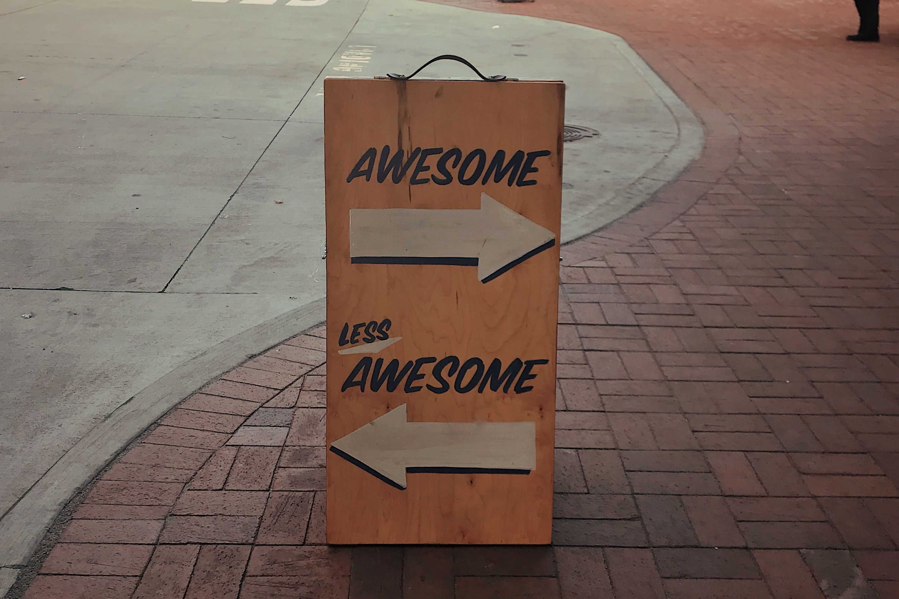 Less awsome Foto einen Straßenschilds. Darauf sind zwei Pfeile in entgegengesetzte Richtungen abgebilden. Auf dem einen Pfeil steht awesome und auf dem anderen Pfeil steht less awesome.