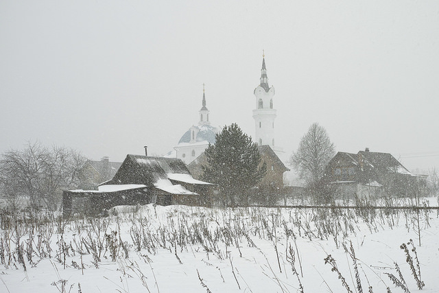 The Church of Archangel Michael in Podzhigorodovo Russian village houses, barns and a church through a snow shower